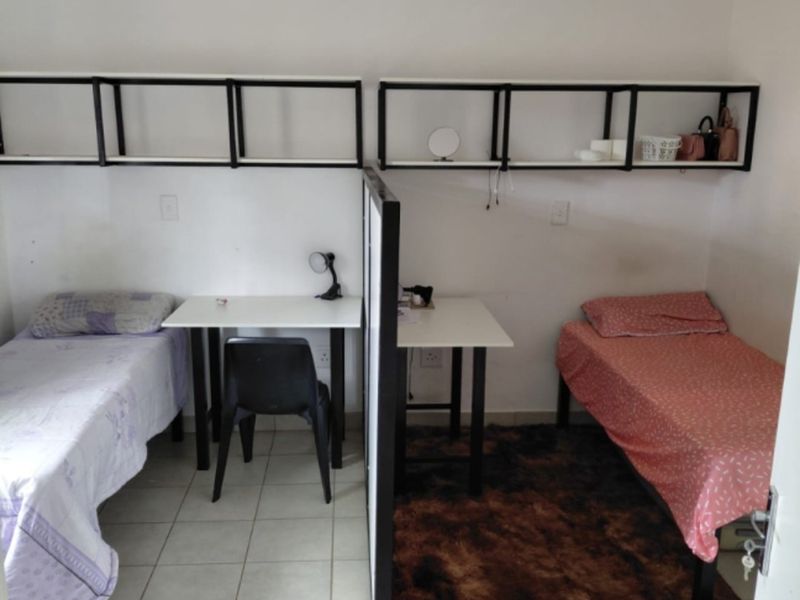 A shared bedroom space featuring tiled flooring, built-in wall shelving units, and a central room divider for privacy between the two sleeping areas.