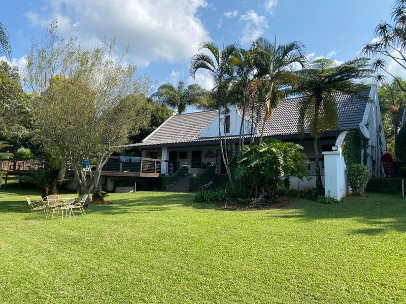 Rear view of the property featuring a spacious lawn, mature garden, and a raised wooden deck attached to the main dwelling.