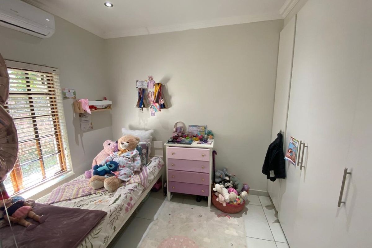 A well-maintained bedroom featuring built-in cupboards, tiled flooring, recessed downlights, and an air conditioning unit.