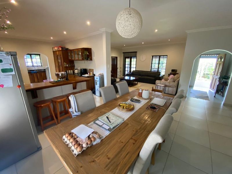 Spacious open-plan living and dining area featuring tiled floors, recessed lighting, and a functional kitchen with wooden cabinetry and a breakfast counter.