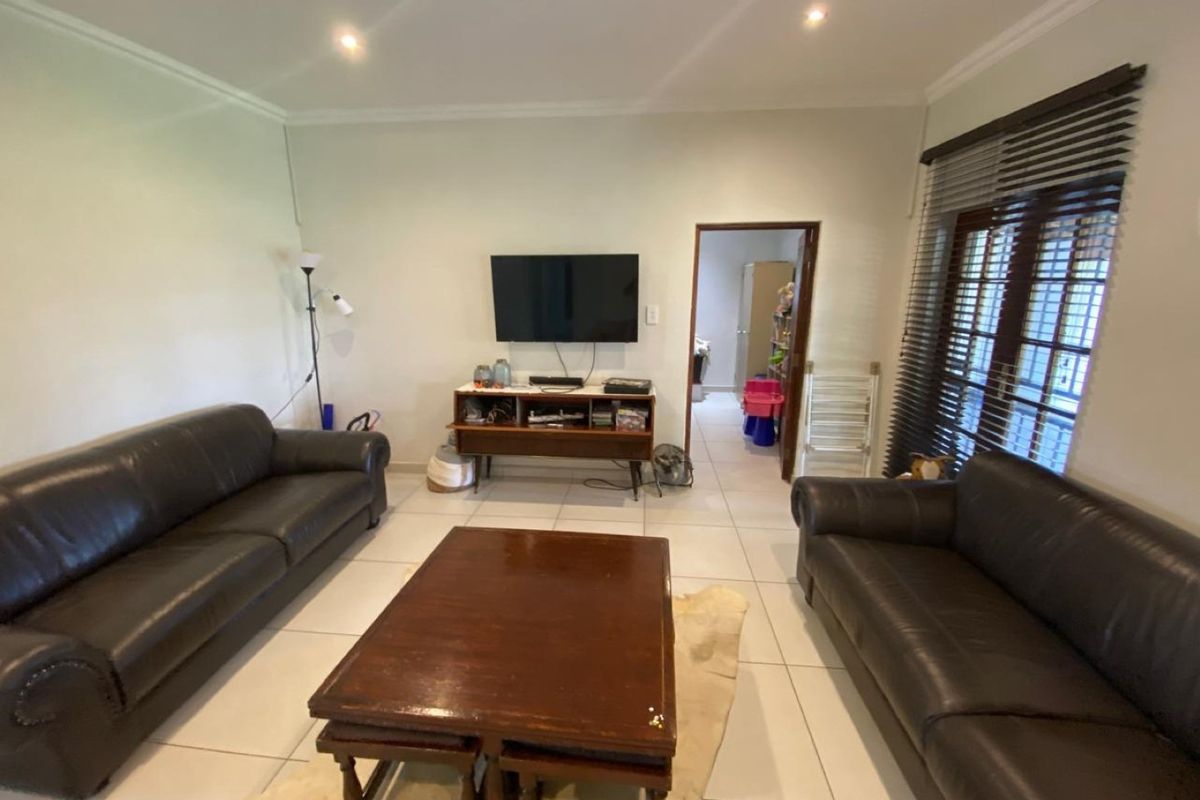 A living room featuring tiled flooring, recessed downlighting, and venetian blinds, providing a functional and neutral space for relaxation.