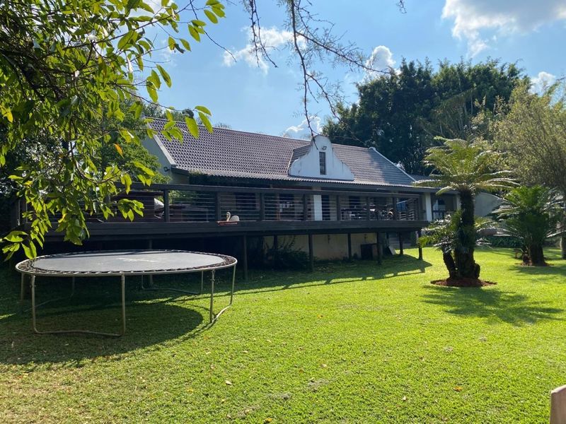 Rear view of the property featuring a spacious raised timber deck with cable railing, overlooking a well-maintained garden and mature trees.
