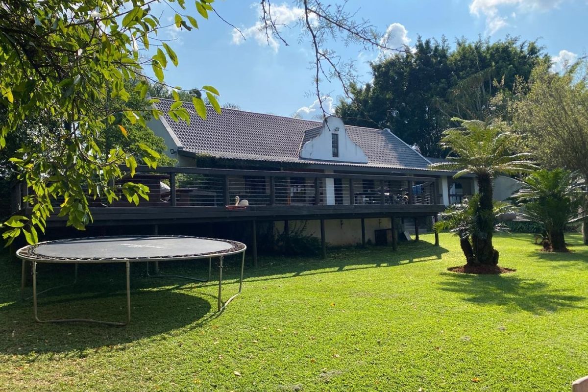 Rear view of the property featuring a spacious raised timber deck with cable railing, overlooking a well-maintained garden and mature trees.