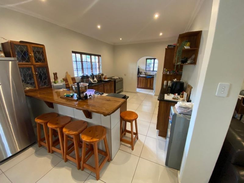 Open-plan kitchen featuring a breakfast bar, tiled flooring, and built-in cabinetry, with an adjoining scullery area visible through the archway.