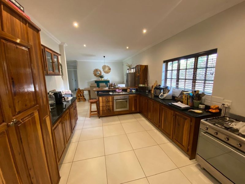 Spacious open-plan kitchen featuring warm wooden cabinetry, granite countertops, and integrated appliances, flowing seamlessly into the adjacent dining area.