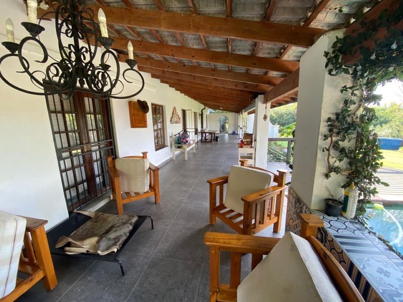 A spacious covered patio featuring exposed timber rafters, tiled flooring, and direct access to the garden area through timber-framed glass doors.