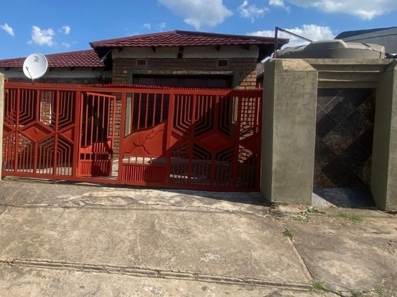 Front exterior view of the property featuring a metal sliding gate, concrete driveway, and brick facade with a tiled roof.