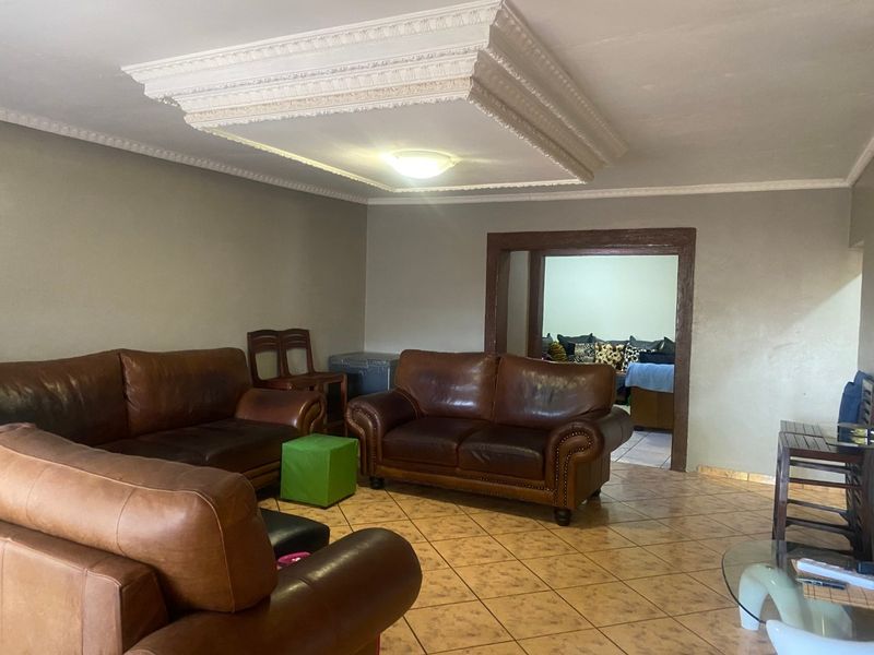Spacious living room featuring a decorative coffered ceiling, ceramic tile flooring, and a wide doorway leading to an adjacent room.