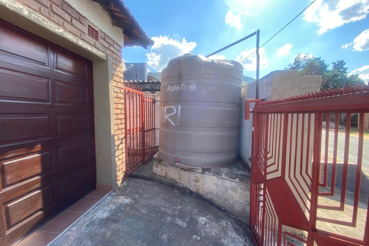 Exterior utility area featuring a large water storage tank on a concrete plinth, adjacent to a garage and secured by metal gates.