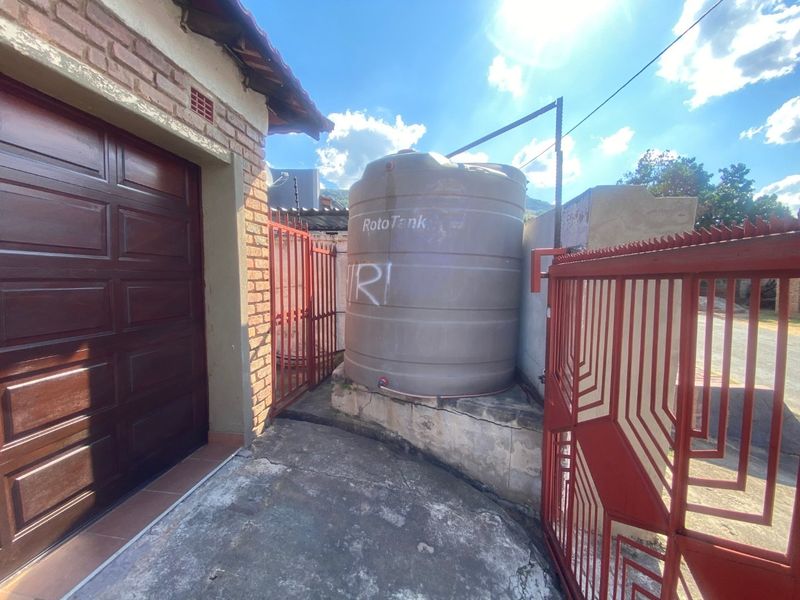 Exterior utility area featuring a large water storage tank on a concrete plinth, adjacent to a garage and secured by metal gates.