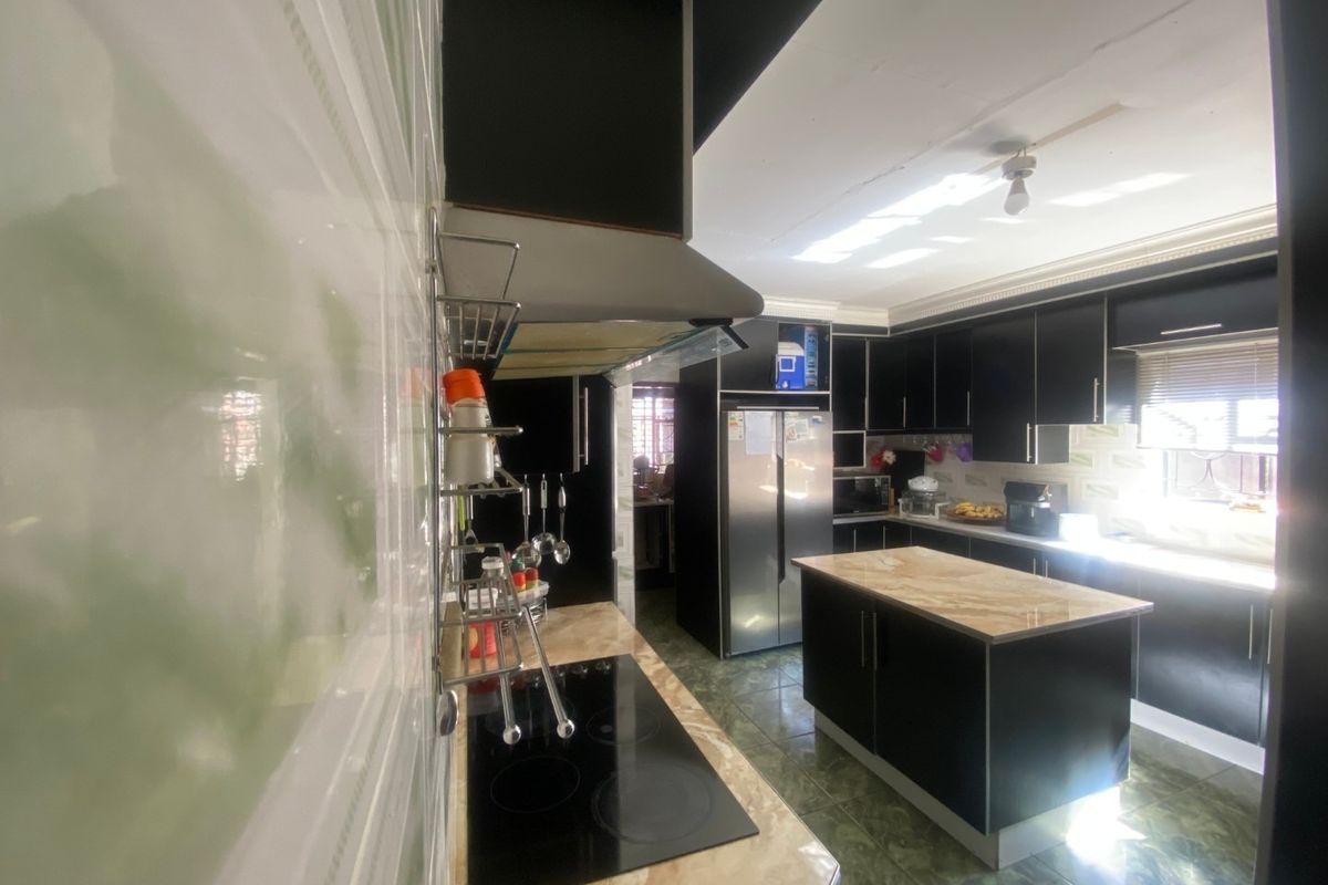 Modern kitchen featuring dark cabinetry, a central island with stone countertops, an integrated hob, and an extractor fan, finished with tiled flooring and backsplash.