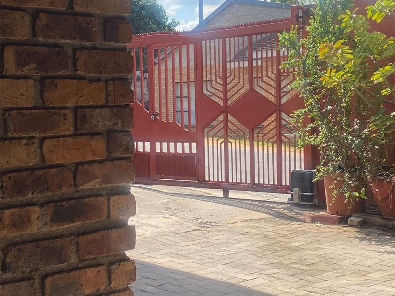 A view of the property entrance featuring a red metal sliding gate, gate motor, and paved driveway.
