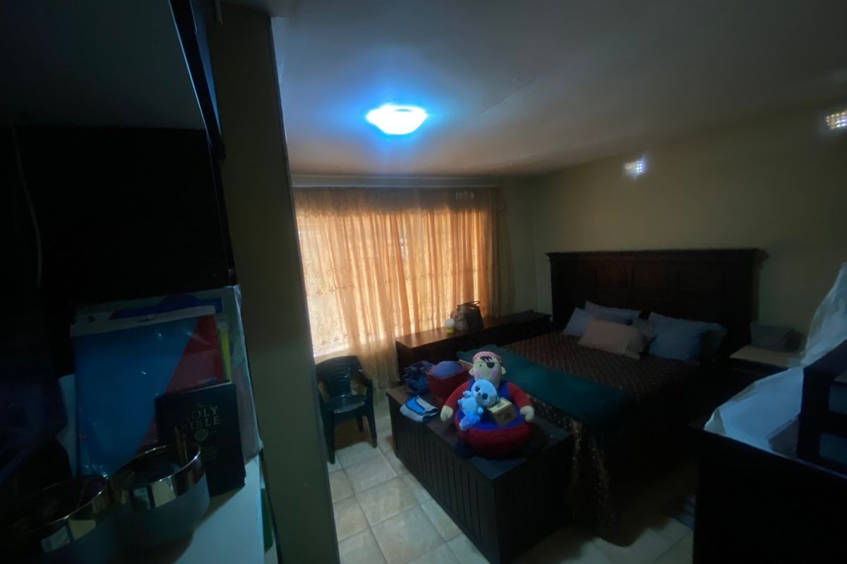 A bedroom featuring tiled flooring and a central ceiling light fixture, with natural light entering through a window covered by curtains.