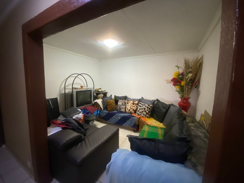 A compact living room featuring tiled flooring and a distinct archway entrance, showing signs of ceiling damage requiring repair.