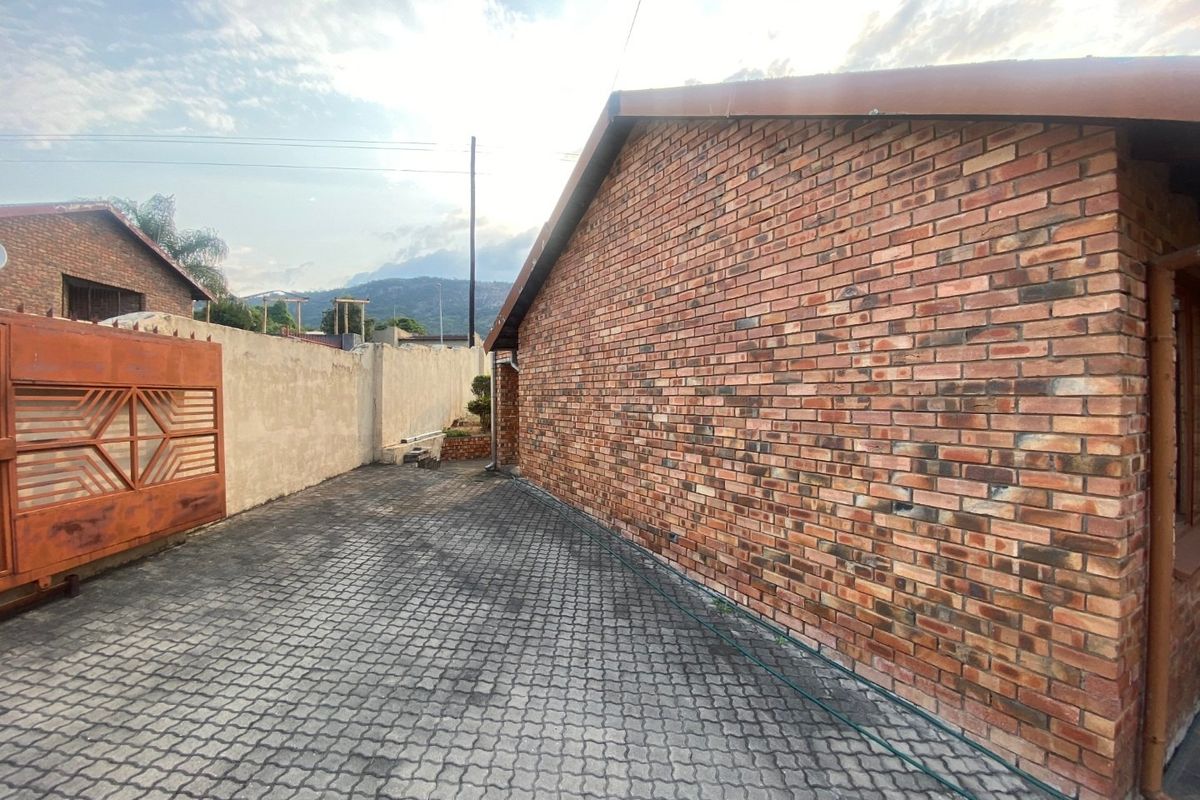 Side exterior view of the property featuring a face brick wall, paved driveway, and secure boundary wall with a metal gate.