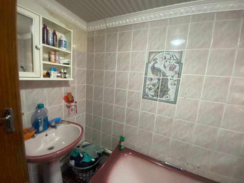 A dated bathroom featuring a pedestal basin, built-in wall cabinet, and a bathtub with decorative wall tiling and crown molding.