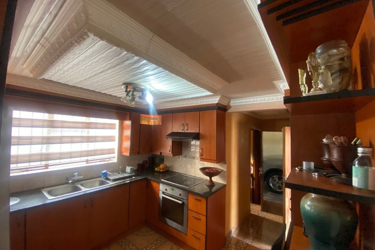 A functional kitchen featuring wooden cabinetry, granite countertops, built-in oven and hob, and decorative ceiling detailing.
