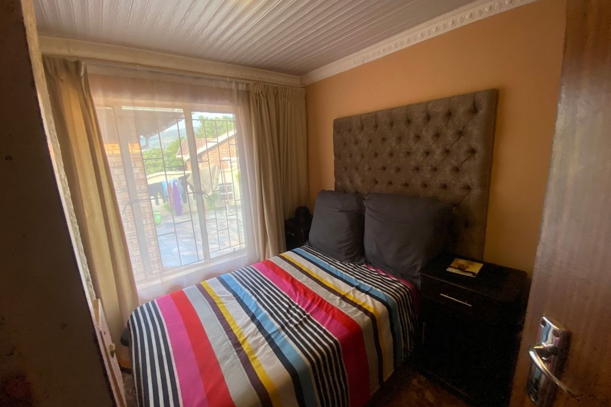 A compact bedroom featuring decorative ceiling cornicing and window security bars, offering a functional space with potential for cosmetic updates.