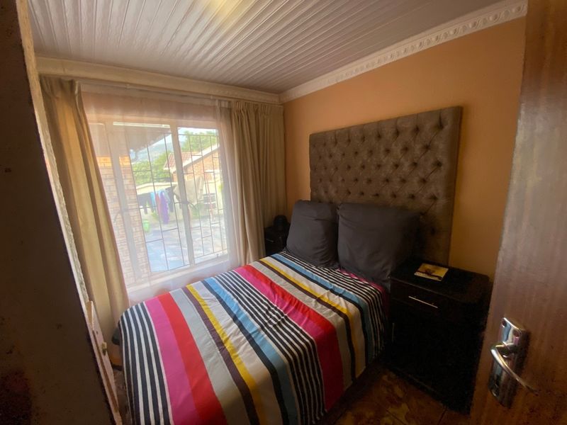 A compact bedroom featuring decorative ceiling cornicing and window security bars, offering a functional space with potential for cosmetic updates.