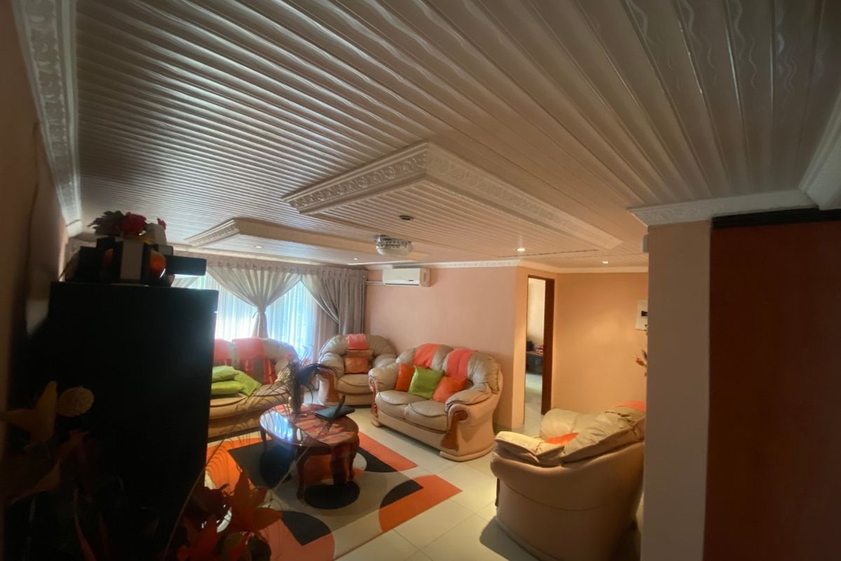 A living room featuring a decorative PVC panel ceiling with recessed lighting, tiled floors, and a wall-mounted split-system air conditioning unit.