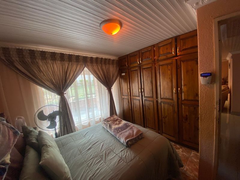A bedroom featuring built-in wooden cupboards, tiled flooring, and classic ceiling paneling, offering a functional and traditional living space.