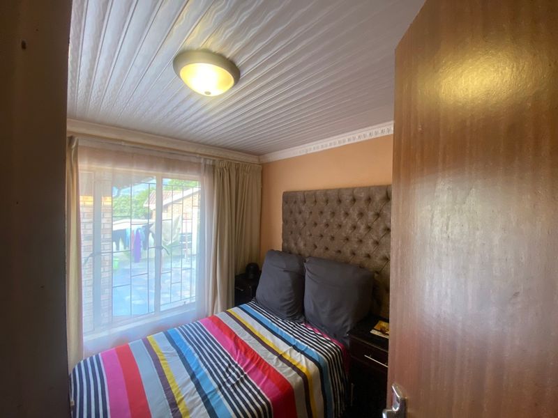 A compact bedroom featuring a window with security bars, a ceiling light fixture, and decorative cornice detailing.