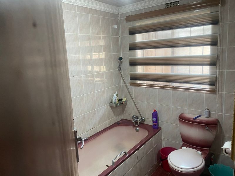 A functional bathroom featuring a built-in bathtub, toilet, and tiled walls. The space would benefit from modern updates to the sanitaryware and finishes.
