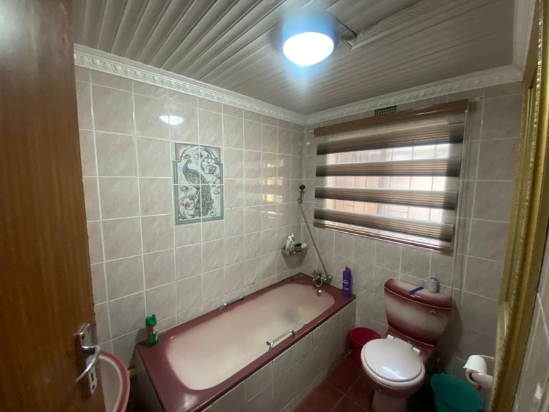 A dated bathroom featuring a built-in bathtub, toilet, and tiled finishes, offering potential for a modern renovation to update the space.