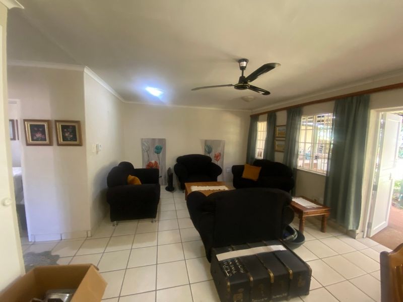 A living room featuring tiled flooring, a ceiling fan, and natural light through windows with curtains.
