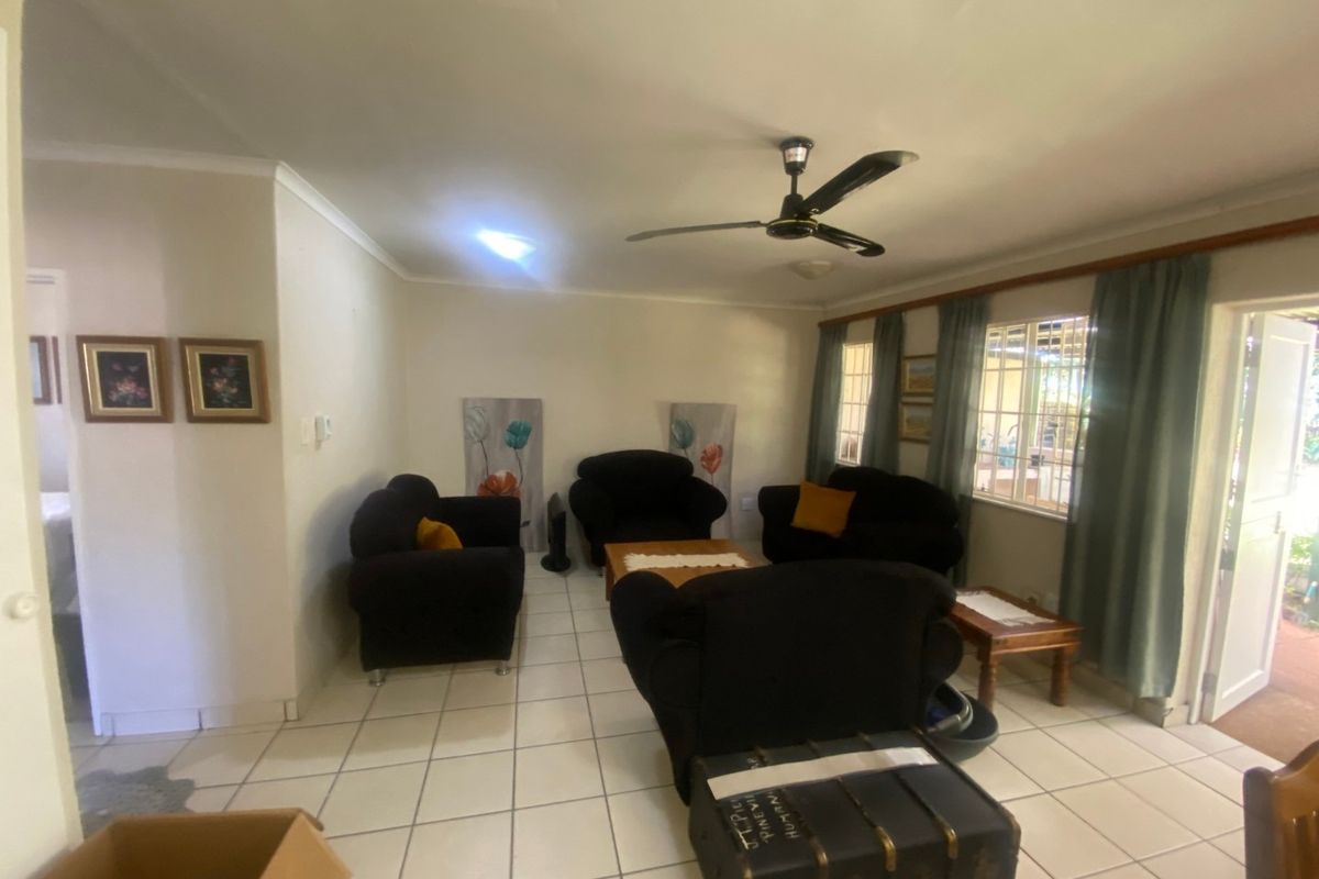 A living room featuring tiled flooring, a ceiling fan, and natural light through windows with curtains.