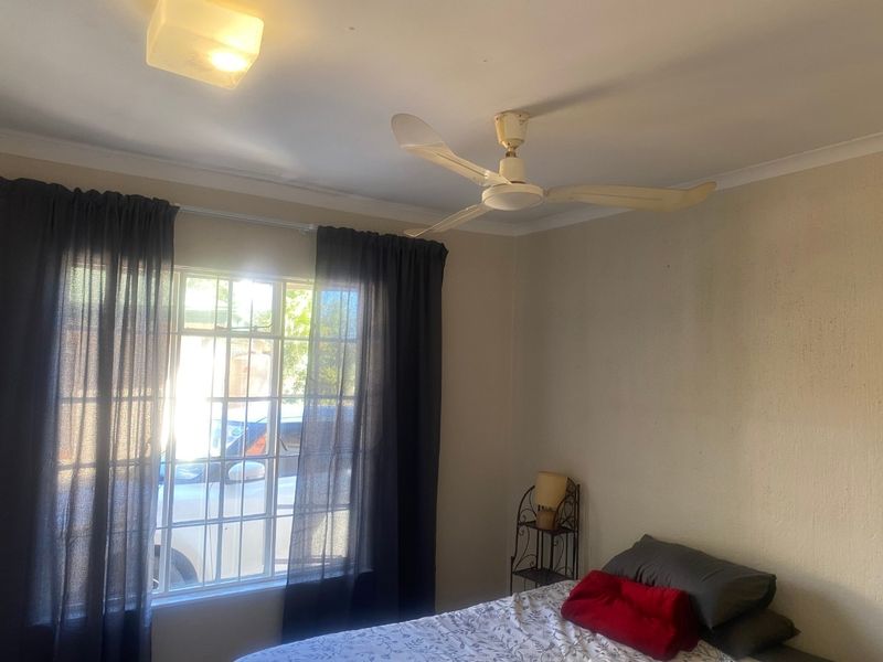 A bedroom featuring a ceiling fan, flush mount lighting, and window security bars, requiring cosmetic updates to the wall finishes.