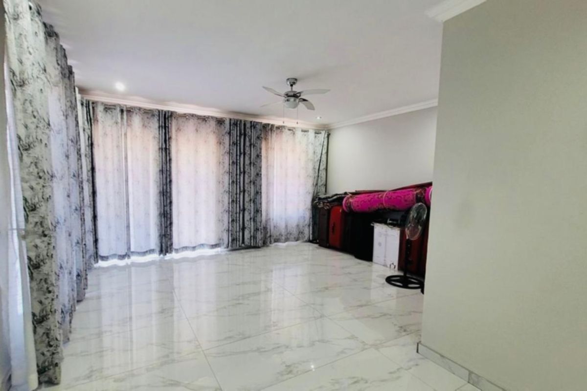 Spacious living area featuring polished marble-look floor tiles, a ceiling fan, and large windows with floor-to-ceiling curtains.