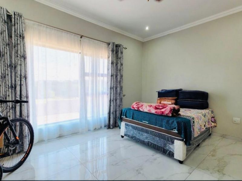 A bright bedroom featuring large windows with curtain rails, polished tiled flooring, and coved ceiling detailing.