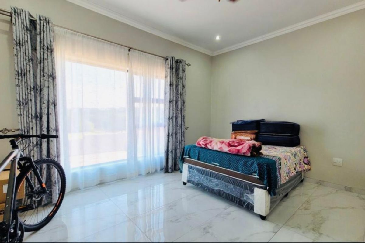 A bright bedroom featuring large windows with curtain rails, polished tiled flooring, and coved ceiling detailing.