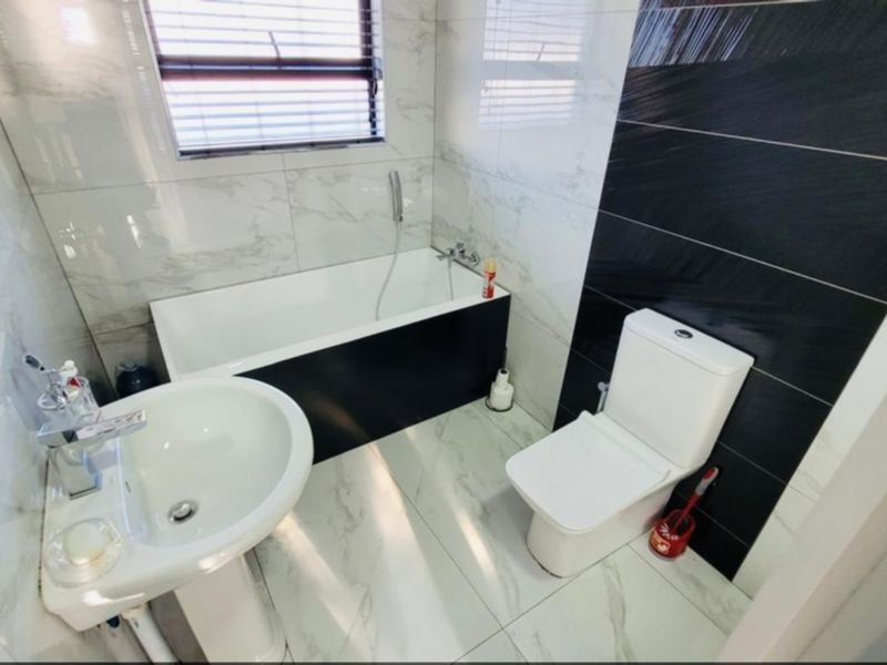Modern bathroom featuring a pedestal basin, built-in bathtub with handheld shower, and toilet, finished with contemporary marble-look and black accent wall tiles.