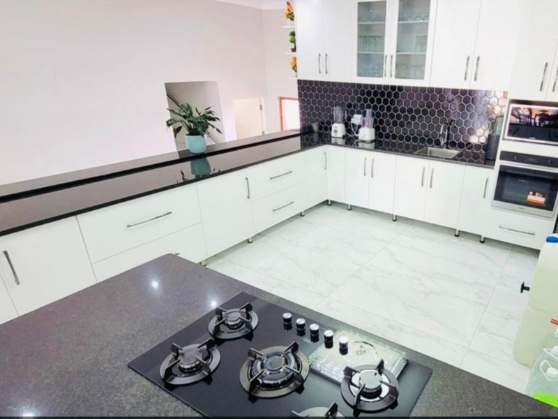 Modern kitchen featuring white cabinetry, black granite countertops, a hexagonal tile backsplash, gas cooktop, and integrated oven and microwave appliances.