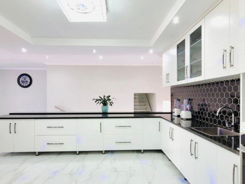 Modern kitchen featuring white cabinetry, black stone countertops, a striking hexagonal tile backsplash, and integrated appliances with recessed lighting.