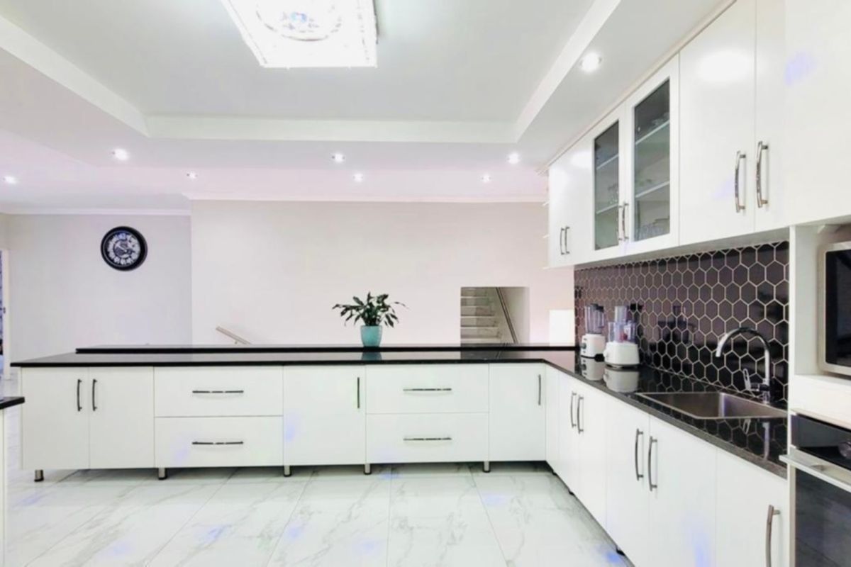 Modern kitchen featuring white cabinetry, black stone countertops, a striking hexagonal tile backsplash, and integrated appliances with recessed lighting.