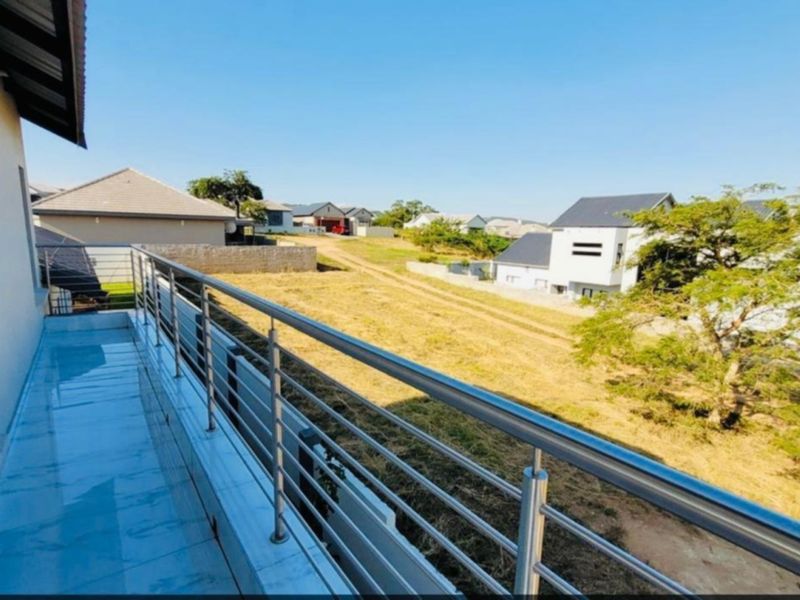 A spacious upper-level balcony featuring modern tiled flooring and a stainless steel balustrade, offering an elevated view of the surrounding residential area.