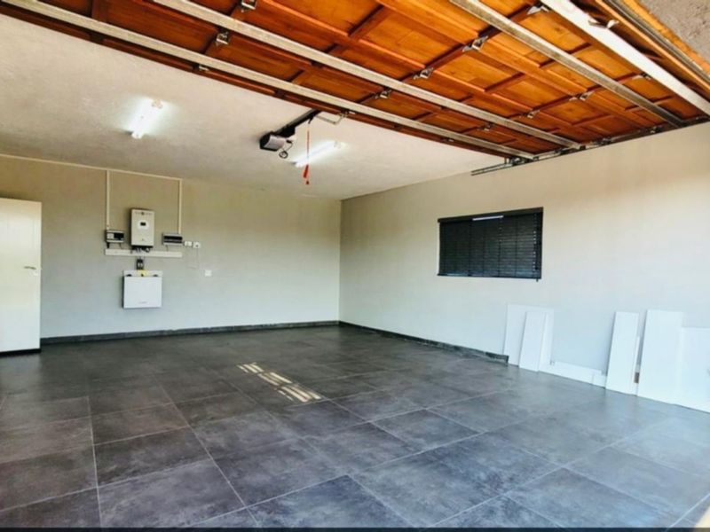Spacious double garage featuring modern tiled flooring, a timber sectional door, and a wall-mounted inverter system.