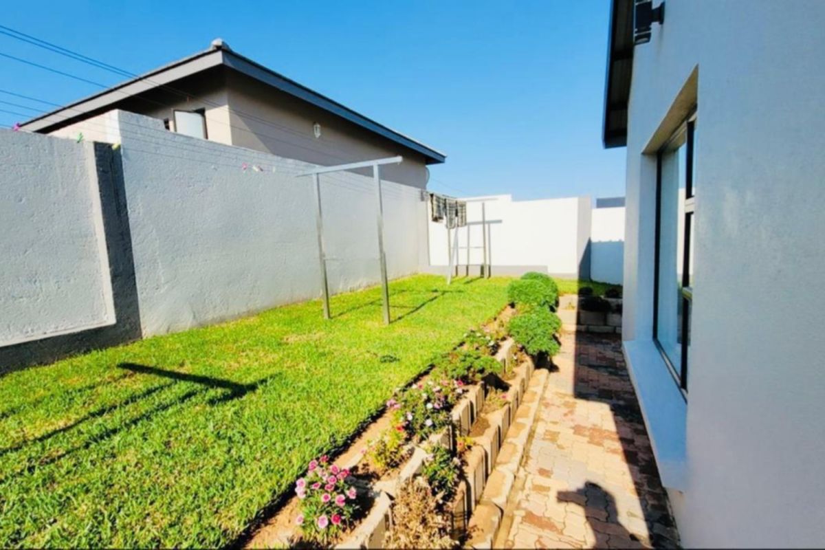 A well-maintained rear garden featuring a paved walkway, a neat lawn, and a retaining wall border along the boundary wall.