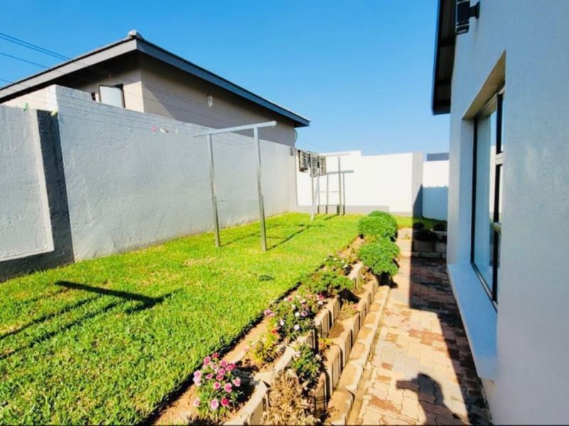 A well-maintained rear garden featuring a paved walkway, a neat lawn, and a retaining wall border along the boundary wall.