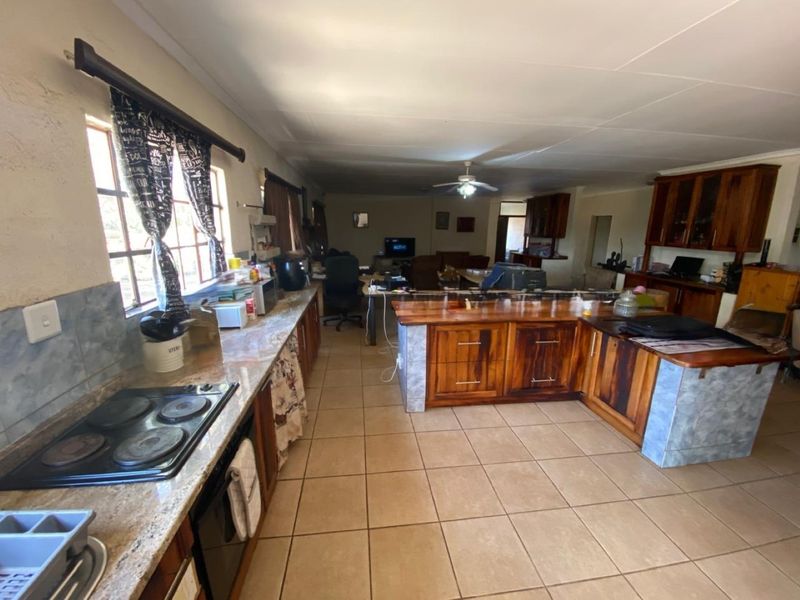 Spacious open-plan kitchen and living area featuring extensive wooden cabinetry, stone-look countertops, and tiled flooring throughout.