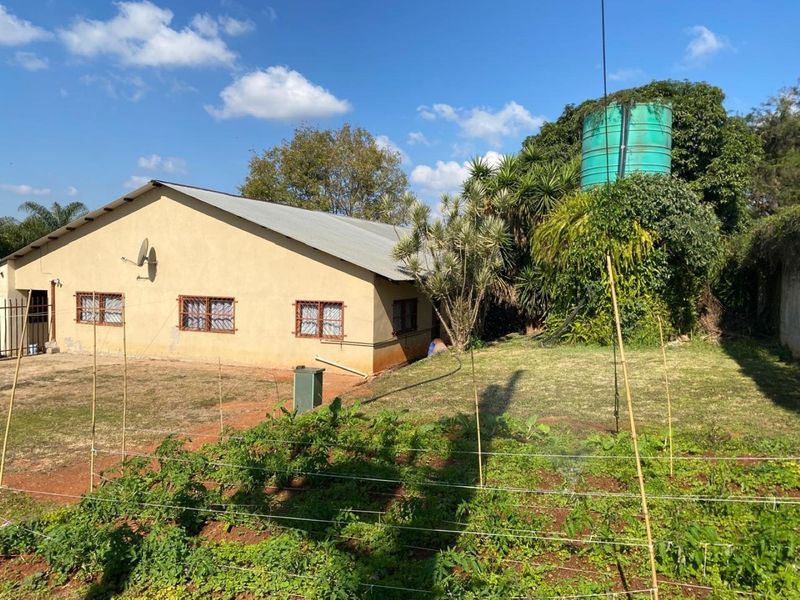 Rear view of the property featuring a metal roof, exterior wall finishes, and a large water storage tank set within a garden area.