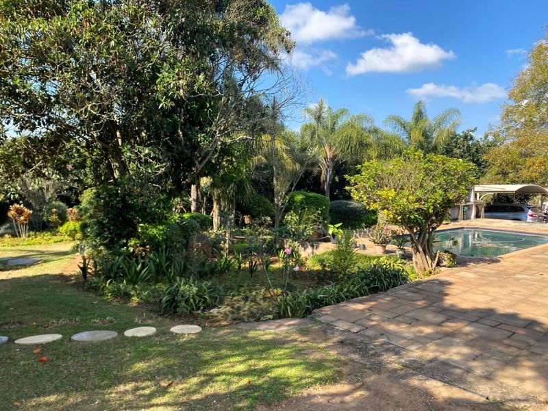 A spacious outdoor area featuring a swimming pool, paved patio space, and established garden landscaping with mature trees.