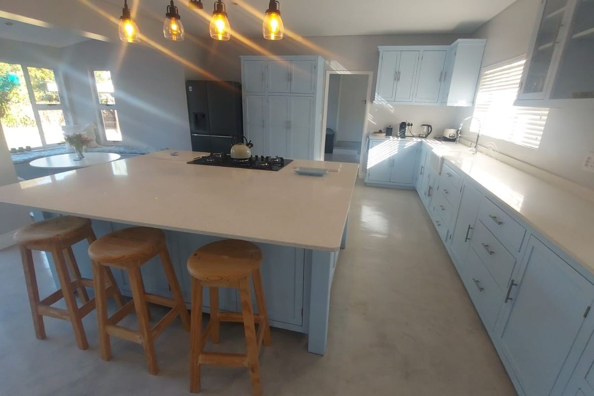 Spacious kitchen featuring a large central island with a gas hob, light blue cabinetry, quartz countertops, and modern pendant lighting.