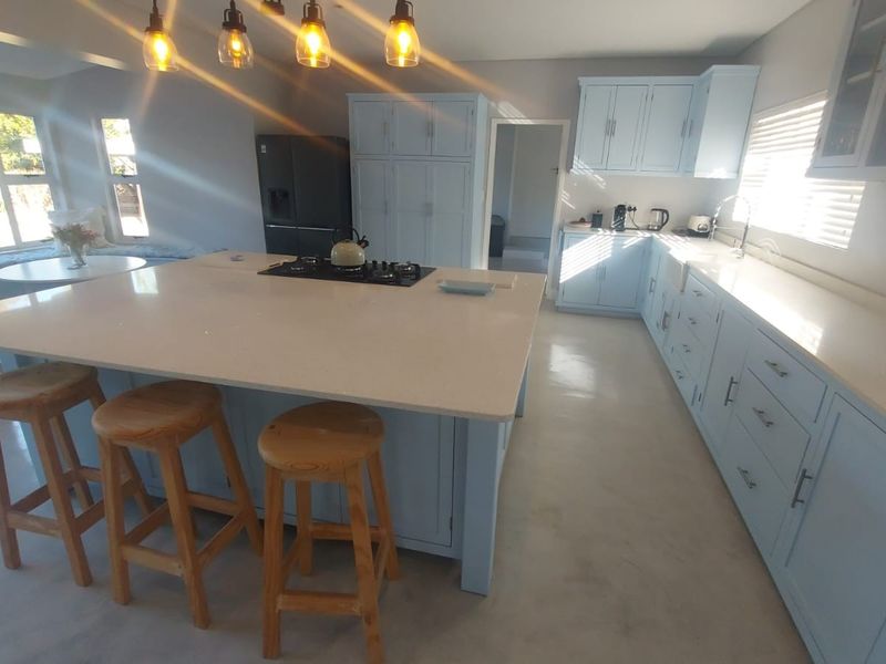 Spacious kitchen featuring a large central island with a gas hob, light blue cabinetry, quartz countertops, and modern pendant lighting.