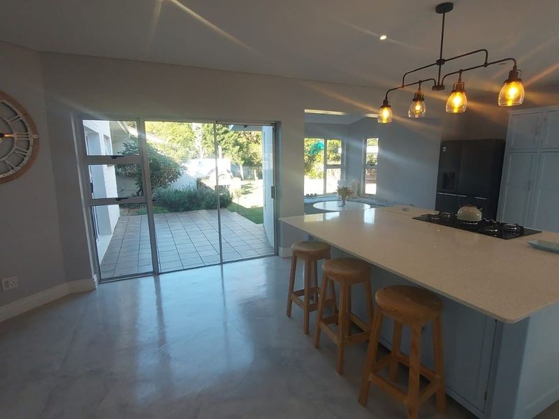 Spacious open-plan kitchen and living area featuring a large island with stone countertops, polished concrete floors, and sliding doors leading to the patio.