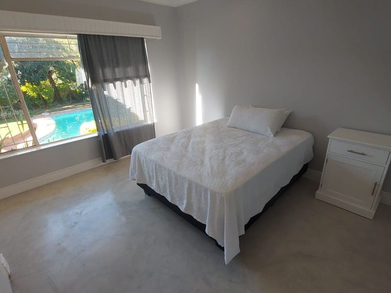 A bright bedroom featuring polished concrete floors and a large window with views overlooking the swimming pool area.