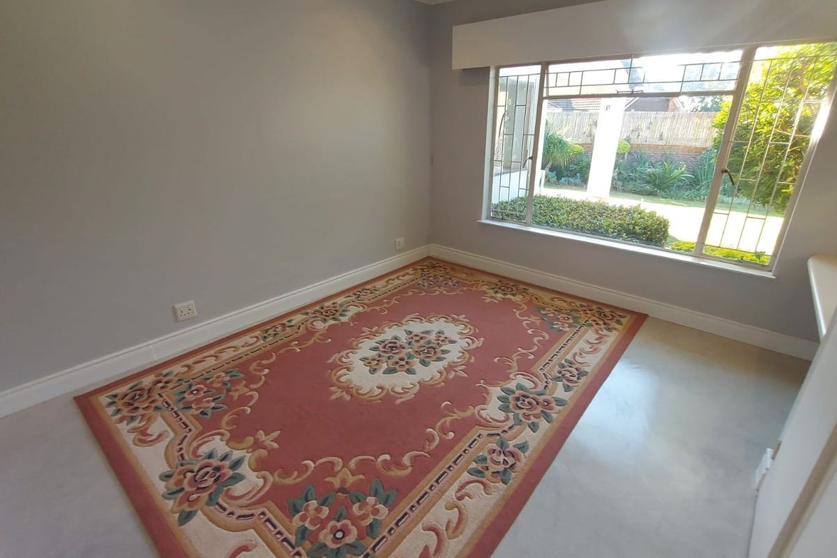 A bright, empty bedroom featuring neutral walls, polished concrete flooring, and a large window with security bars overlooking the garden.